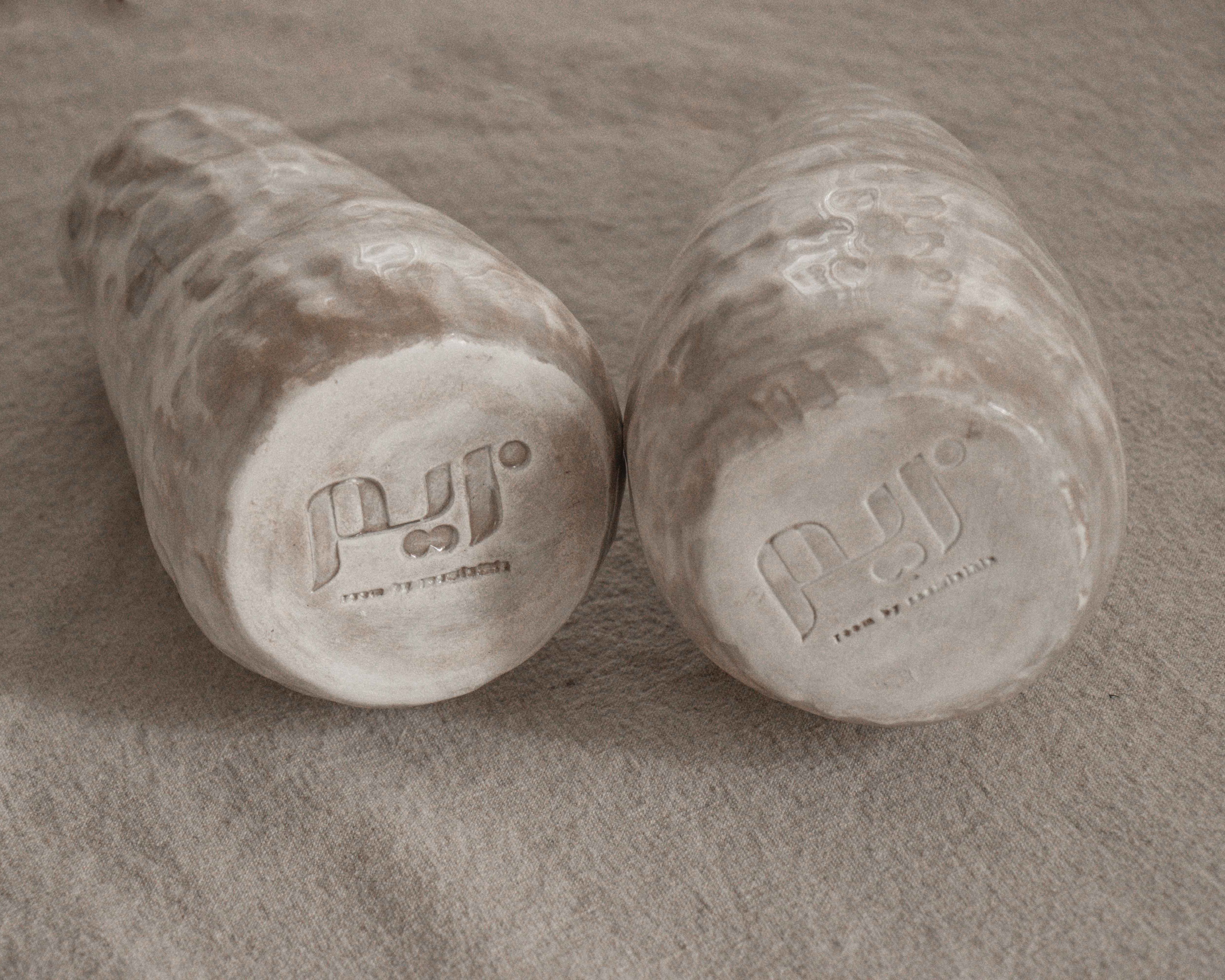 Two cylindrical ceramic sculptures and vases with branding on a textured surface