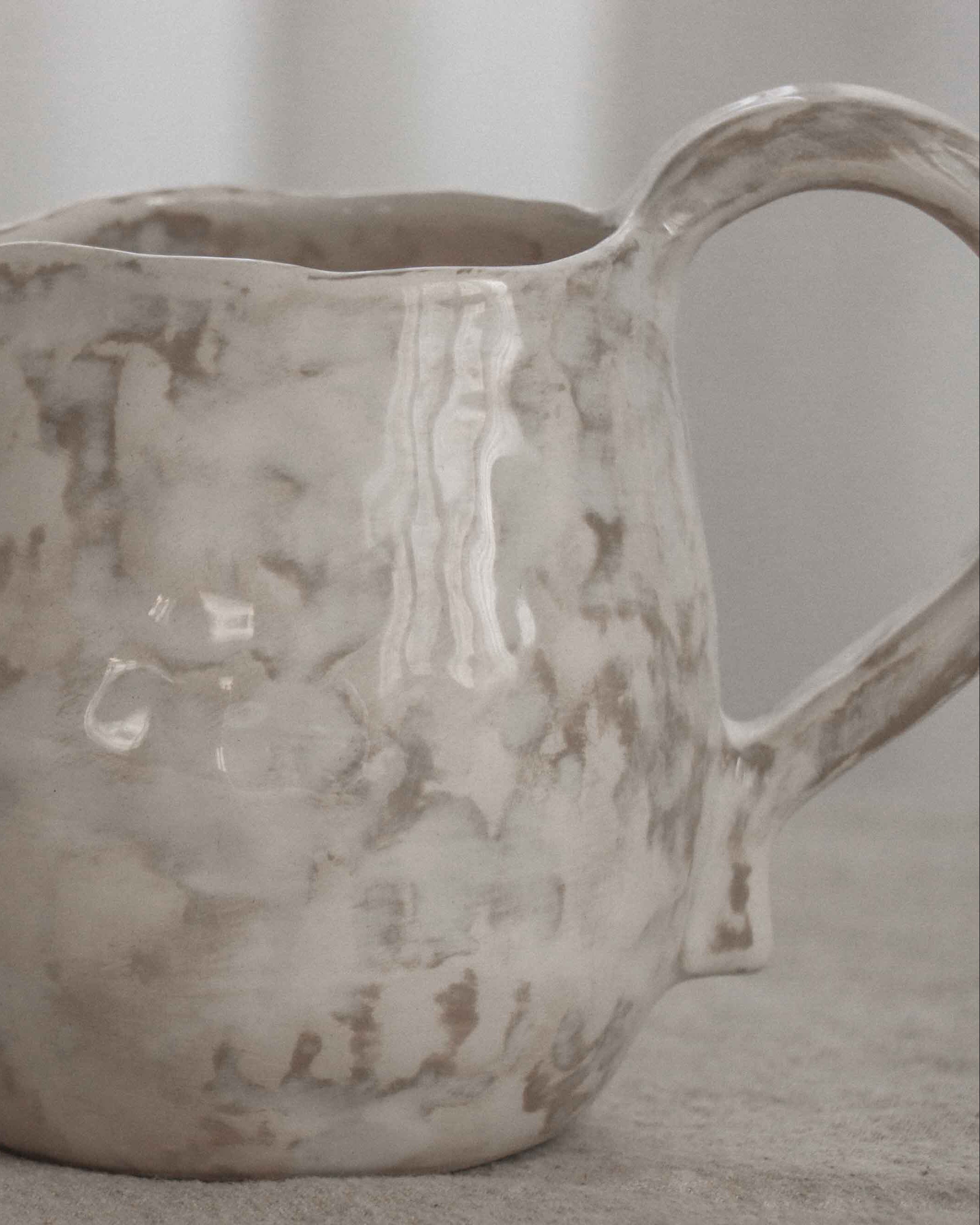 White ceramic pitcher with a handle on a neutral background
