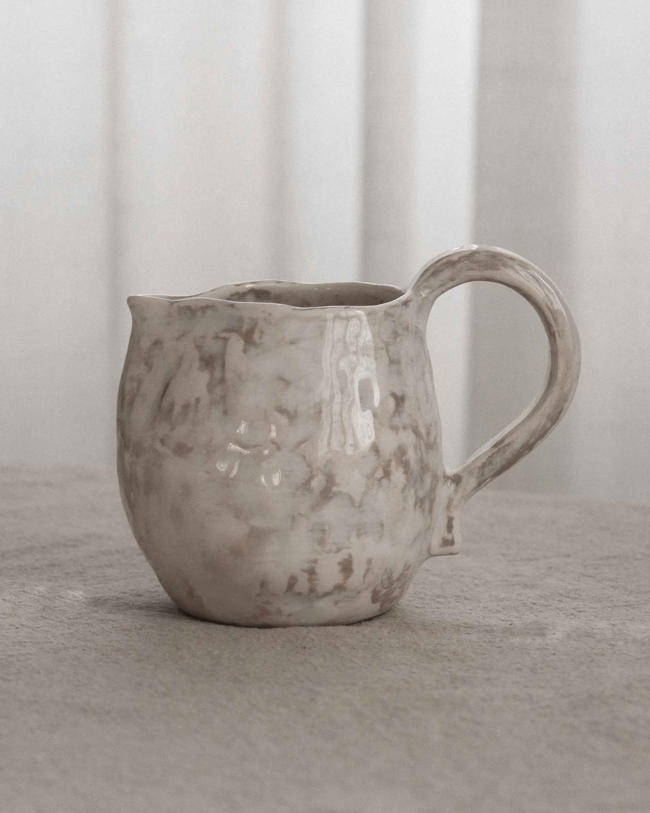 Ceramic pitcher on a textured surface with a neutral background
