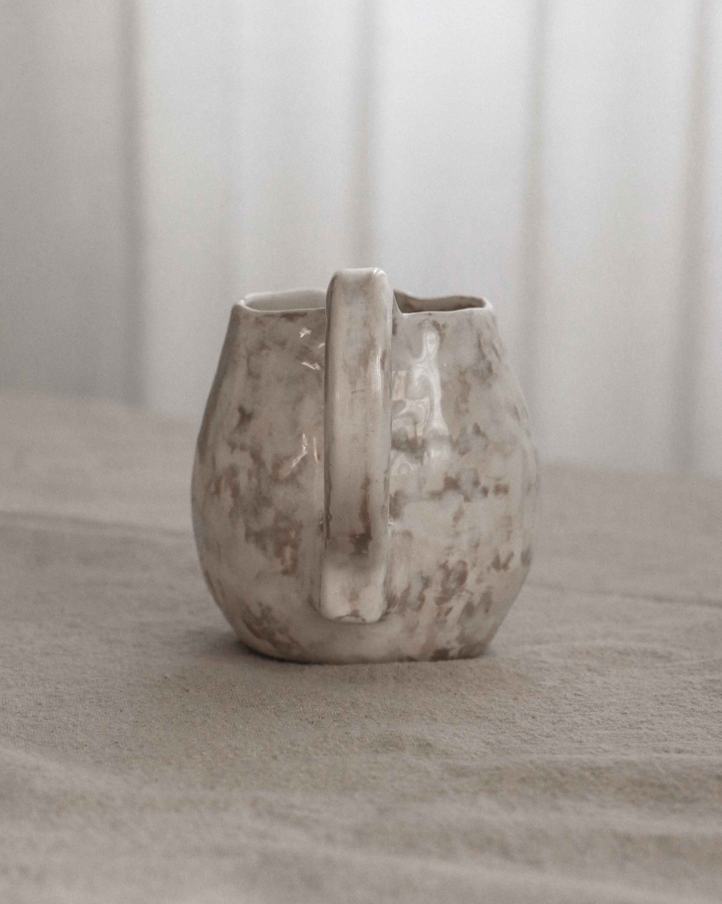 Ceramic pitcher on a textured surface with a neutral background