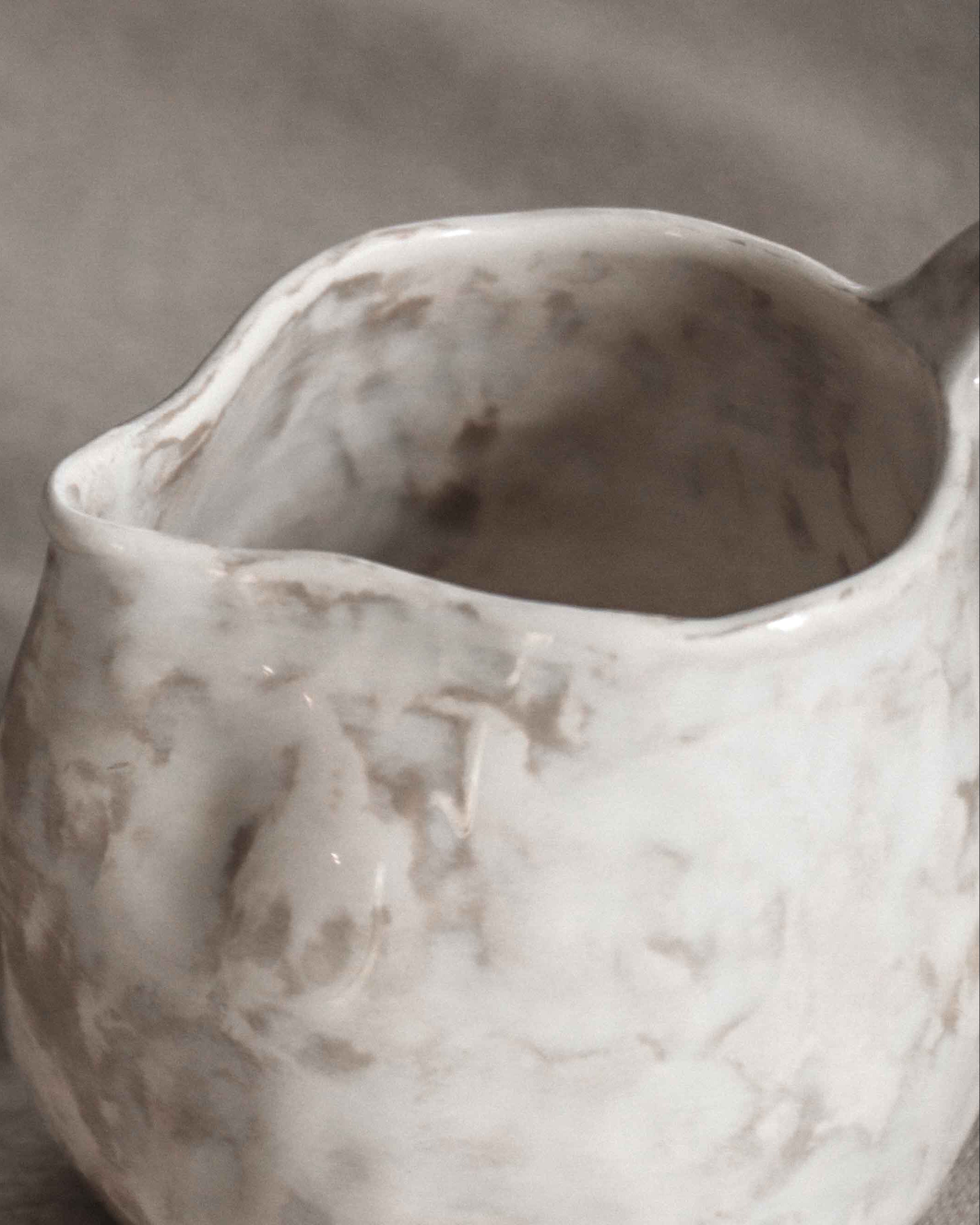 Close-up of a textured ceramic pitcher on a gray fabric background