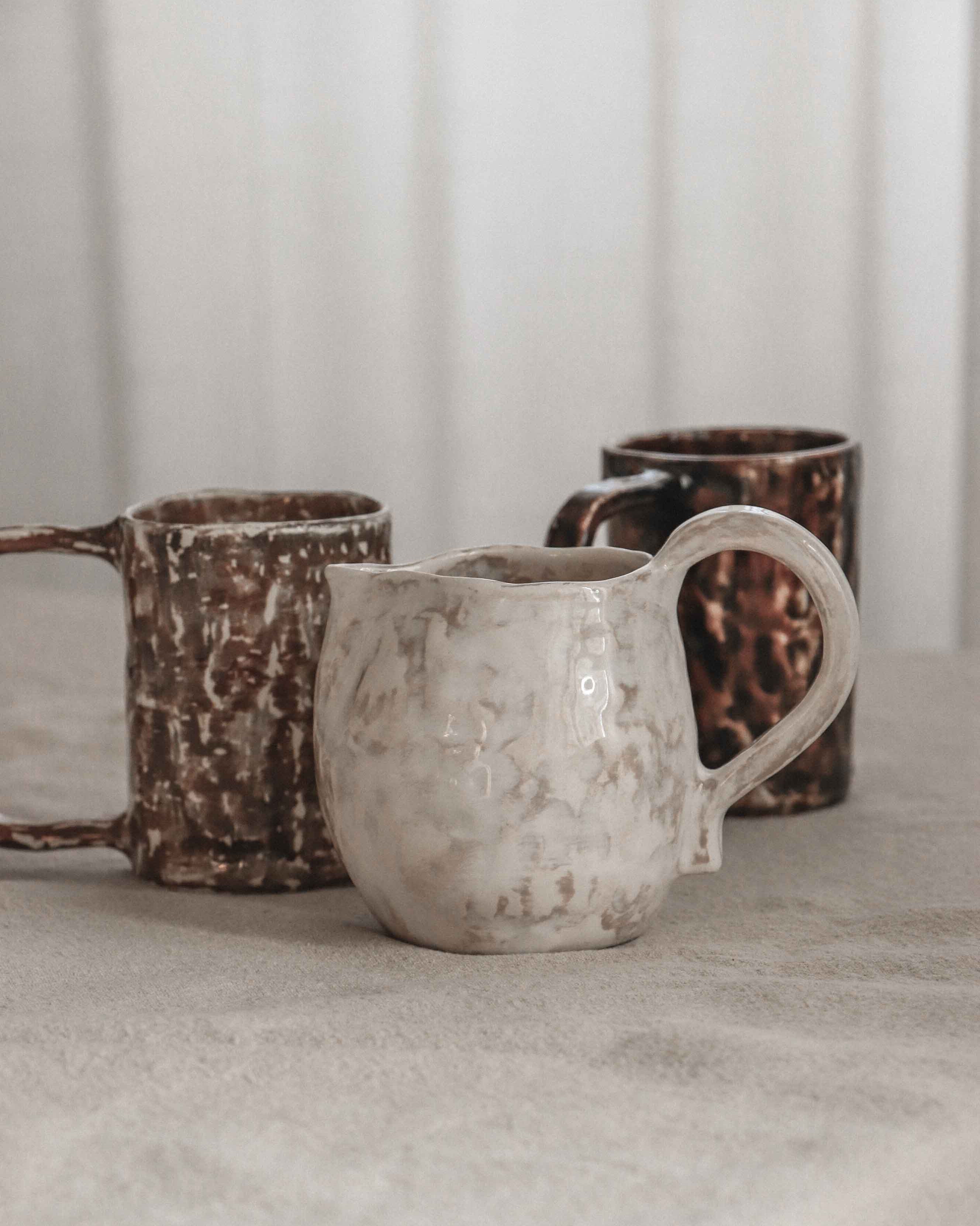 Three ceramic mugs on a neutral surface with a blurred background