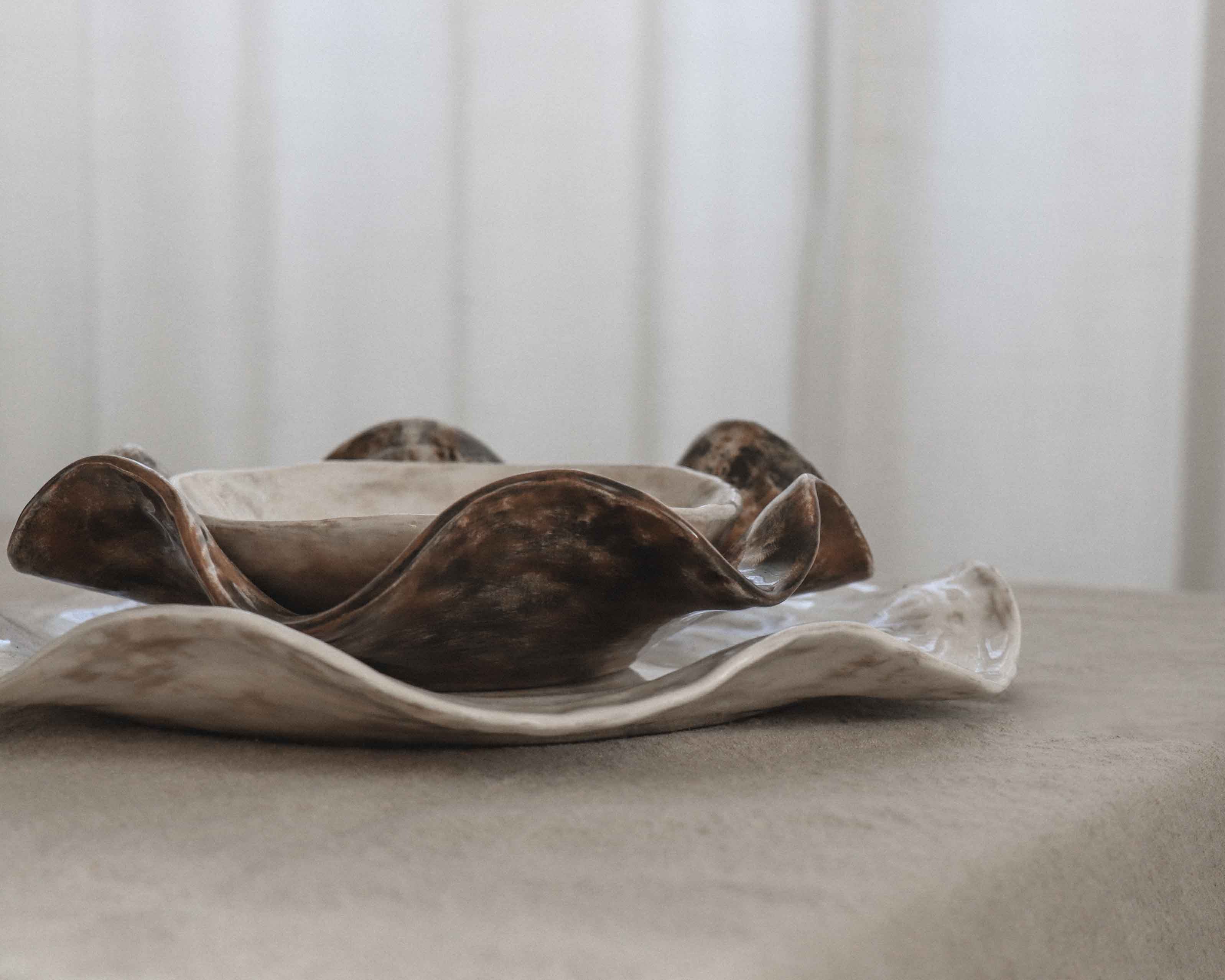Decorative ceramic bowl and ceramic plate on a neutral surface with a blurred white curtain background