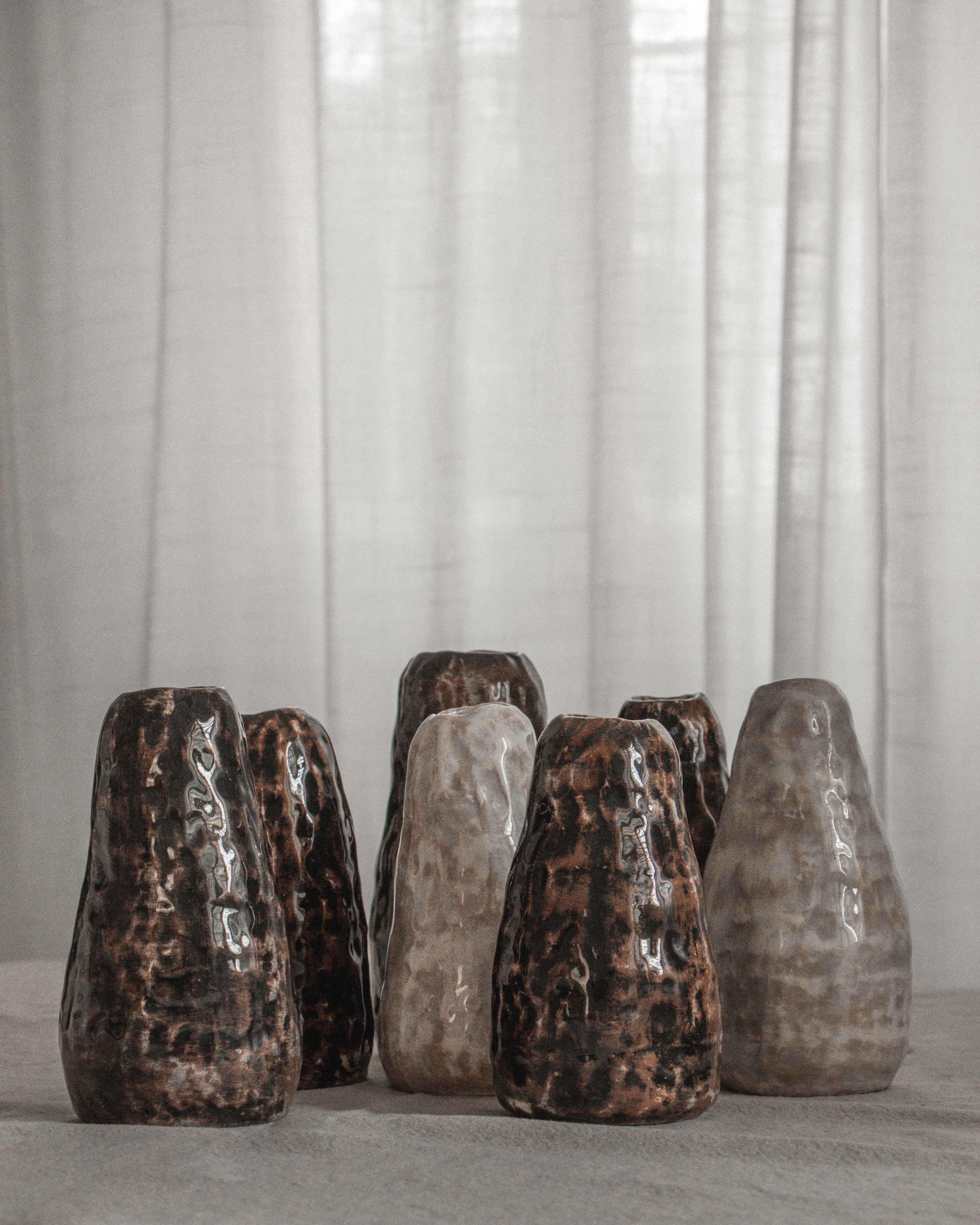 Set of ceramic vases with textured finishes on a neutral surface with light curtains in the background.